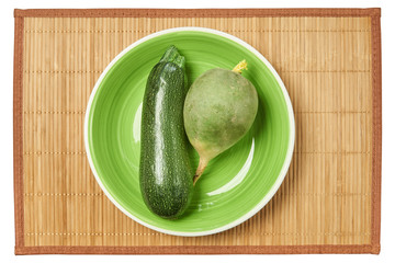 bright patterned green zucchini and pale green radish on the same green plate on a cane place mat