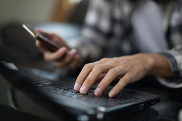 a man typing laptop computer while using a mobile phone to contact his client at home. writing and doing a homework while taking an online class.