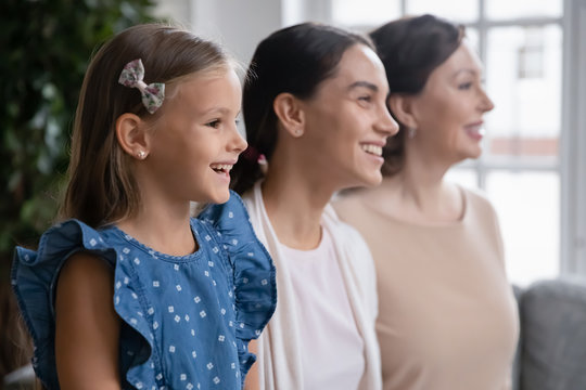 Profile view of overjoyed three generations of women look in distance smiling visualizing together, happy little girl with young mom and senior grandmother pose for picture at home, unity concept
