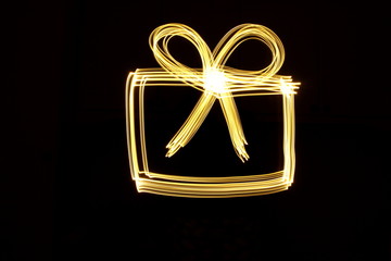 Long exposure photograph of neon gold colour in the shape of a present, gift box outline against a...