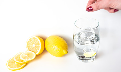 girl dips a pill with vitamin C in a glass of water. Nearby are lemons