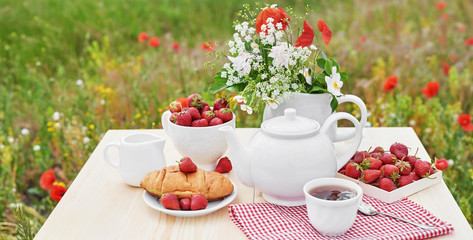 Romantic Valentines french or rural breakfast: tea, strawberries, croissants on table in poppy field. Countryside and Cozy Good morning weekend concept. Background with copy space. Date outdoors