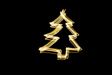 Long exposure photograph of neon gold colour in an abstract Christmas tree shape outline, parallel lines pattern against a black background. Light painting photography.
