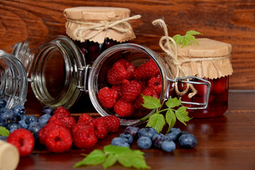 Blueberries and raspberries spill out of old glass jars