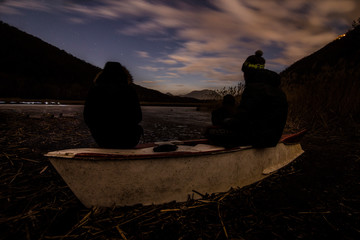Rear View Of Friends Sitting On Broken Boat During Sunset