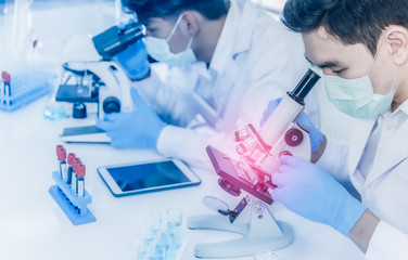 Asian scientist team wear medical face mask and working by using microscope