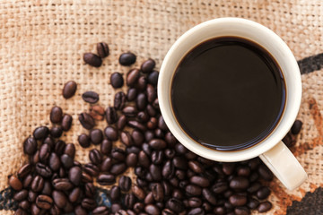 Cup of coffee and roasted coffee beans are on jute bag