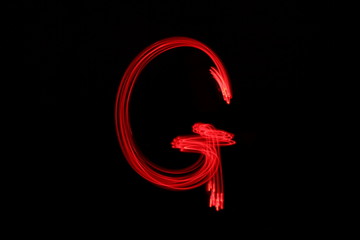 Long exposure photograph of the letter g in neon red colour fairy lights against a black...