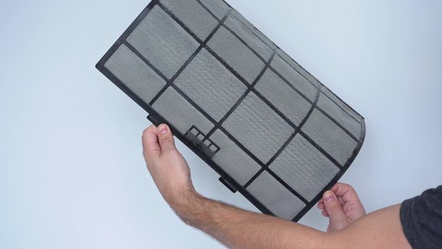 A man examines a terribly dirty air conditioning filter. He removed the filter from the air conditioner and twists it in his hands. Air conditioning service.