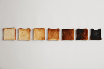 Tasty toasted slices of bread from unroasted to burnt. Stages of toastiness. Selective focus. Crusty delicious snack. White background. Set of toasts each toasted for longer time, degree of roasting.