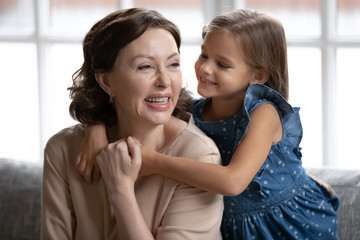 Loving little preschooler girl hug show care and gratitude to smiling mature 60s grandmother, cute small granddaughter embrace smiling grandparent, feel grateful thankful, enjoy tender moment at home