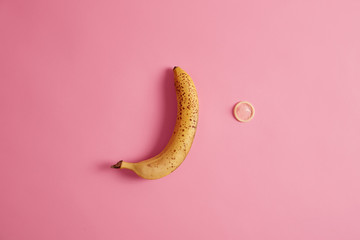 Intimacy concept. Yellow ripe banana and condom on pink background. Contraception and safety....