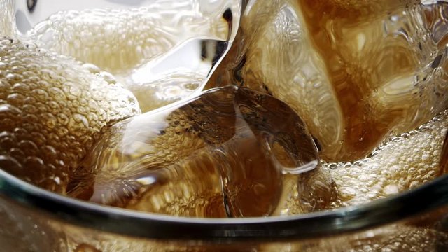 Coca Cola pouring into the glass with beautiful ice cubes. Refreshing drink, soda. Bubbles on the surface. 