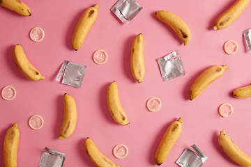 Contraception, erotic concept. Yellow bananas and unwrapped condoms around. AIDS awareness. Flat lay composition. Safe relationships. Pink background. Protect yourself. Prevention of venereal disease