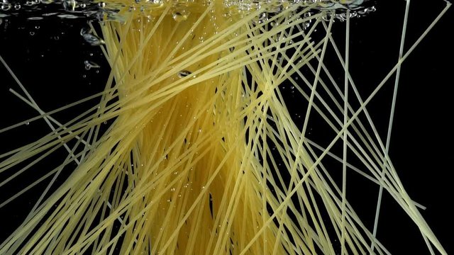 Pasta throwing in the boiling water. Spaghetti boiling. Cooking italian dish. Black background. Slow motion