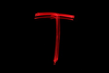 Long exposure photograph of the letter t in neon red colour fairy lights against a black background. Light painting photography. Part of an alphabet series. 