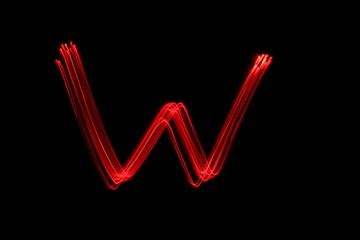 Long exposure photograph of the letter w in neon red colour fairy lights against a black background. Light painting photography. Part of an alphabet series.  © LizFoster