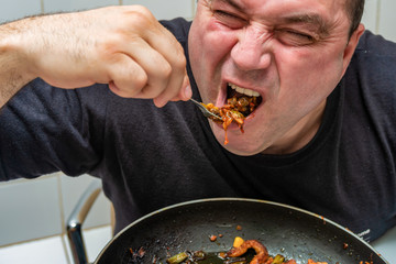 A hungry man eagerly eats fried meat with sauce from a fork.