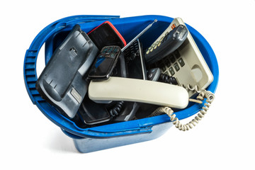 Fototapeta premium Old desk phones, cordless phone, cell phones and smartphones in a trash can isolated on a white background.