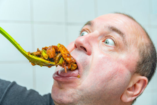 A crazy man with bulging eyes looks at fatty and junk food, sending it into his mouth. The concept of obesity and eating.