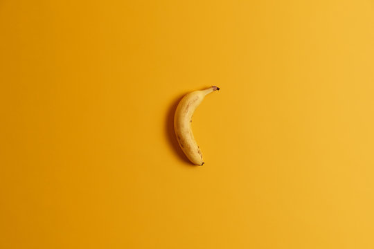 Top view of one ripe banana isolated over yellow background. Delicious tropical fruit for your tasty breakfast or snack. Ready to eat whole banana. Useful nourishing product rich in vitamins