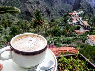 Cup with latte on a saucer. Against the background of wooded mountains and a village in the mountains