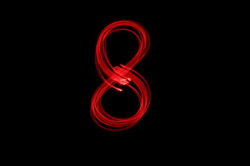 Long exposure photograph of the number 8 in neon red colour fairy lights against a black background. Light painting photography. Part of a number series. 
