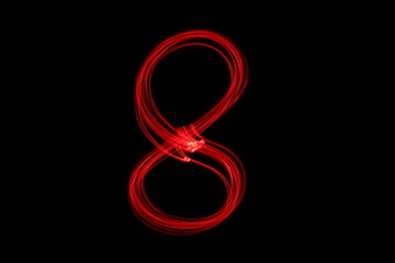 Fototapeta premium Long exposure photograph of the number 8 in neon red colour fairy lights against a black background. Light painting photography. Part of a number series. 