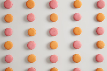 Round french macaroons arranged in rows against white background. Multicolored traditional sweet dish containing much sugar. Delicate flavor. Food and desserts concept. Delicious cookies to eat