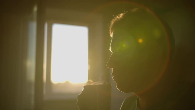 Silhouette of a man with a mug of hot fresh steam coffee over a mug, sun flare, camera movement