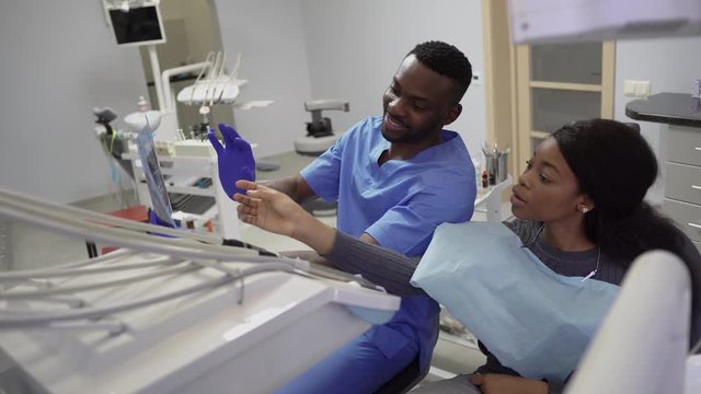 Dentisry concept, healthcare, oral and teeth care. Young handsome african man dentist discusses the strategy of treatment with the patient african charming young lady, showing xray image of jaws
