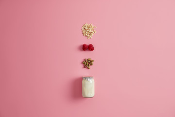 Glass jar of yoghurt, pistachio, red raspberry and cereals to mix together and eating. Pink background. Healthy diet breakfast. Natural ingredients for porridge or quick snack. Vegetarian meal