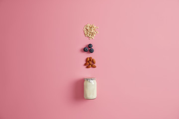 Variety of healthy ingredients for healthy breakfast. Yoghurt, oatmeal cereals, blueberry, almond nut to mix on pink background. Delicious products to prepare yummy nutrient porridge. Eating concept