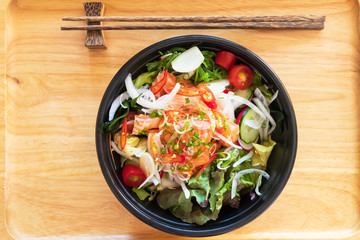 Spicy salmon salad with herbs; delicious fusion food. Top view on wooden tray with chopsticks. 