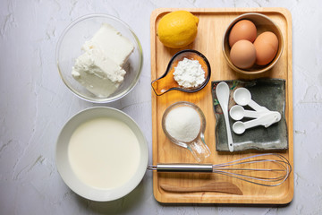 Baking ingredients for cheesecake on wooden tray. Eggs, flour, sugar, lemon, cream, creamcheese and kitchen utensils on table.