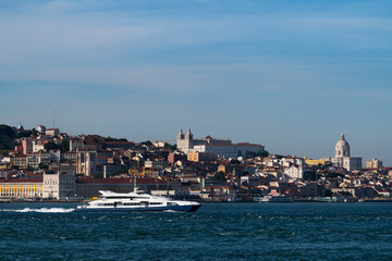 Naklejka premium A passenger boat crossing the Tagus River (Rio Tejo) with the skyline of the downtown of the city of Lisbon on the background, in Portugal, Europe