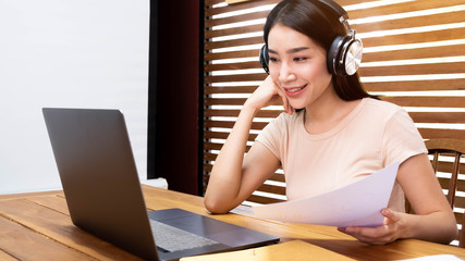 Asian girl in headphones sit at desk watch webinar making notes, happy biracial young woman in earphones work study using computer.