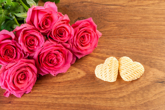 Composition of pink roses and two hearts on a brown wooden background