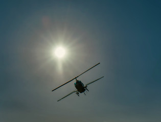 Fototapeta na wymiar A helicopter with an agricultural spray bar silhouetted by a bright sun.