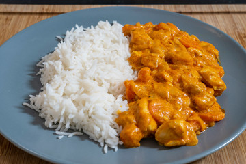 Plate of white rice with chicken and curry sauce on a wooden table.