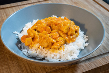 Plate of white rice with chicken and curry sauce on a wooden table.
