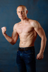 Portrait of strong healthy handsome Athletic Man Fitness Model wearing jeans posing near dark blue wall