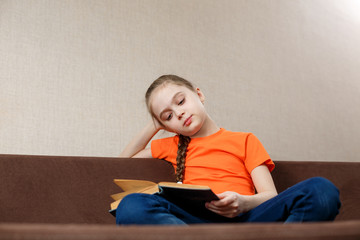 Portrait of nice attractive lovely focused cheerful teen girl wearing orange t-shirt sitting in lotus pose in sofa at home