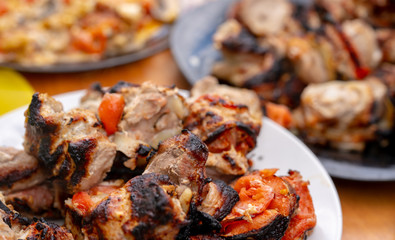 Close up of toasted shashlik on plate. Succulent barbecue with tomatoes on table. Concept of picnic outdoor.
