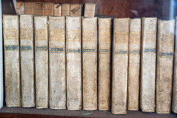 A dusty shelf with a group of old antique publications. A series of white covered books with 253 numbers and golden written text title OPERE DEL METASTA - TOM
