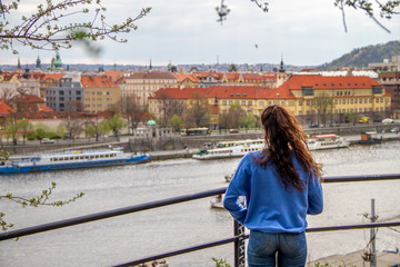 Young girl with a blue sweater watching a city landscape with a beautiful river from a beautiful viewing point surrounded by a frame of beautiful plants and flowers