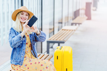 Stylish young woman blogger influencer traveler in straw hat makes selfie while sitting at a public...