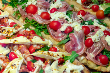 Big pizza pieces with various topping in an Italian restaurant. Colorful slices with juicy bacon, fresh red tomato, green vegetables, hard / soft white cheese, pepper seeds, salami