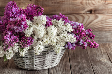 Spring composition lilac flowers in a basket on a wooden background.
