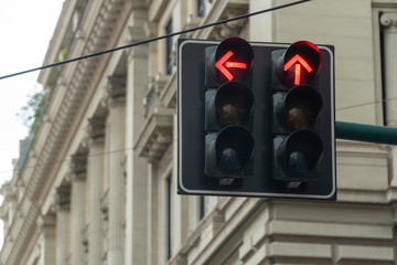 An automated traffic light in the city turned red. Arrow signs are showing straight and left directions to stop.